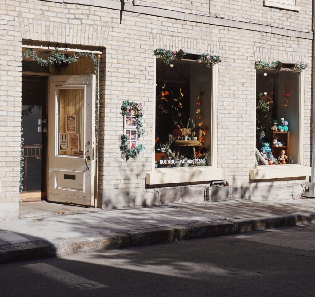 Sunlit exterior of a quaint boutique and cafe, with festive decorations and large display windows.